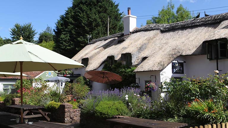 The postcard-worthy frontage of the Farmers Arms in Combe Florey with thatched roof, pretty flowers and outside seating