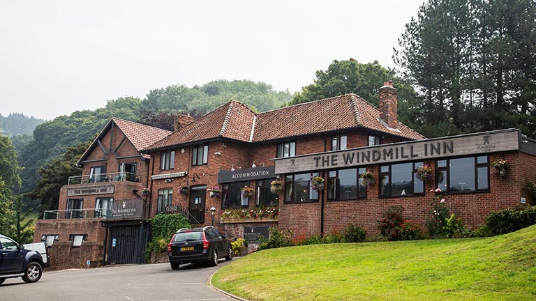 The pretty exterior of the Windmill Inn in Williton with wooded hills in the background