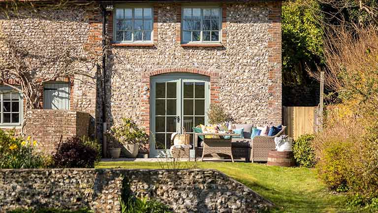 A beautiful garden with outdoor seating in front of a stone cottage in Sussex