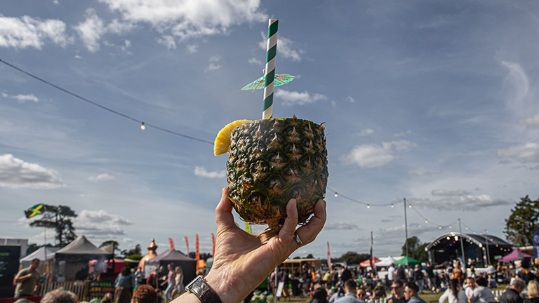 A juicy pineapple drink held up against a blue sky at Foodies Festival