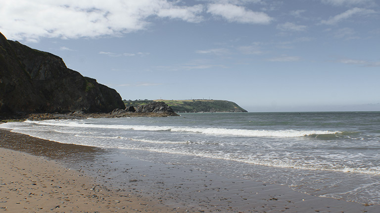The sandy shores of Tresaith beach lapped by sea on a sunny day