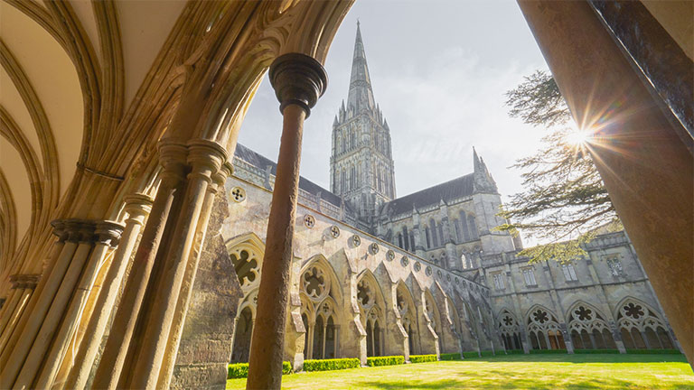 A beautiful view of the outside corridors, archways and spire of Salisbury Cathedral in the sunshine