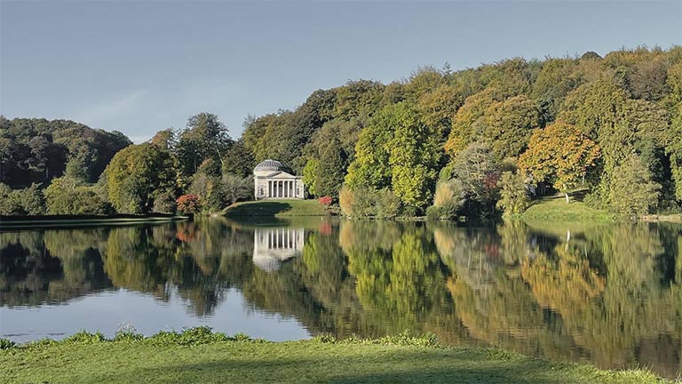 One of the beautiful lakeside temples within Stourhead's grounds on a blue sky day in Wiltshire