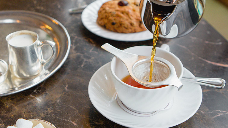 A cup of loose leaf tea being poured into a cup through a strainer, accompanied by sweet treats, at Betty's in Harrogate in Yorkshire