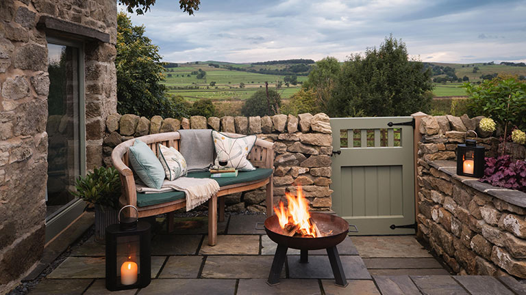 A love seat in the garden of Hartley Hare in Settle with countryside views and a crackling fire pit